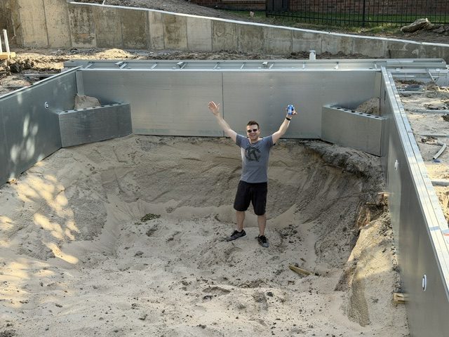 Kevin standing in the empty pool with arms raised and a beer in hand