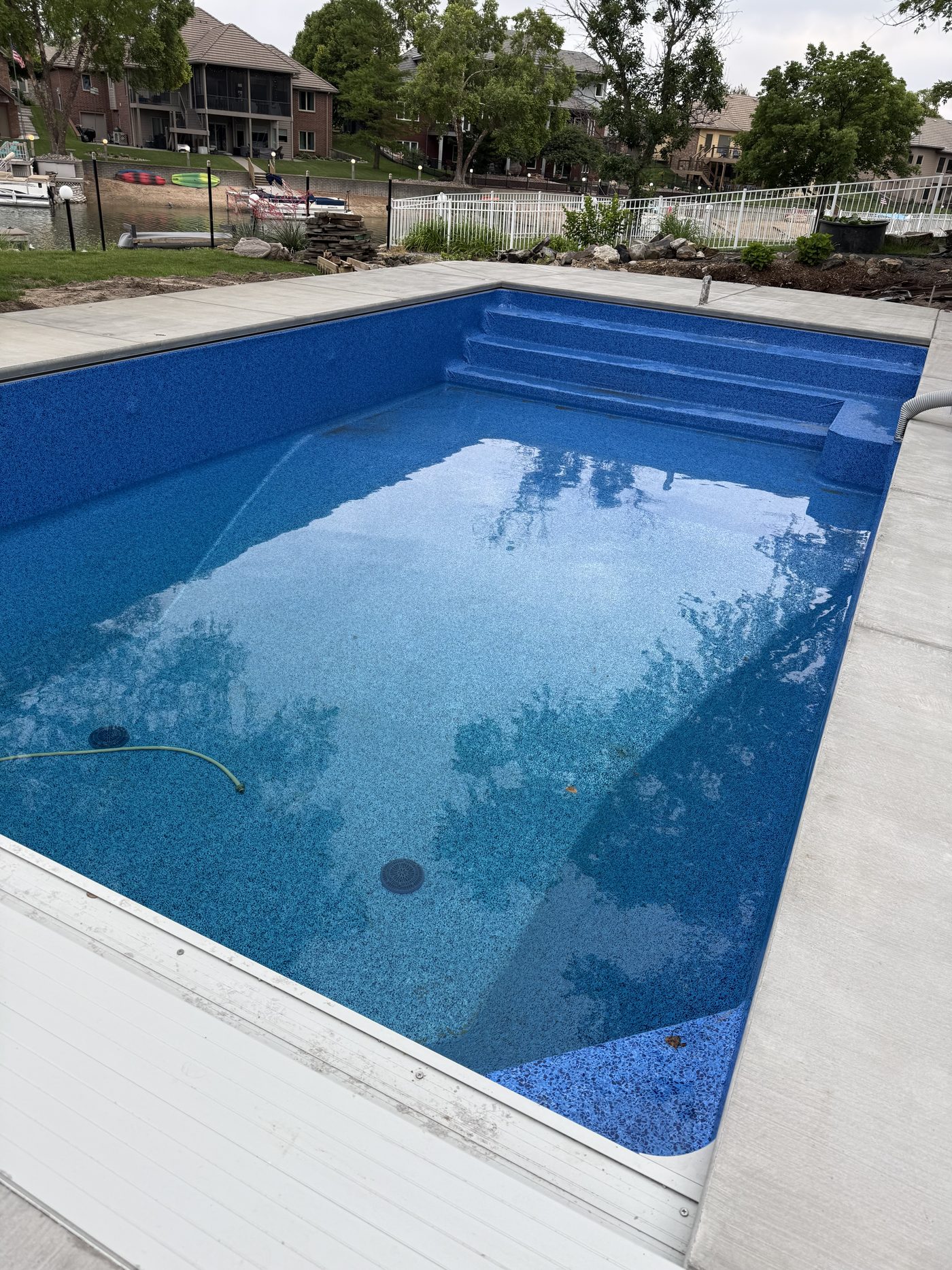 The finished pool with blue liner installed and water filling, deck complete, lake behind